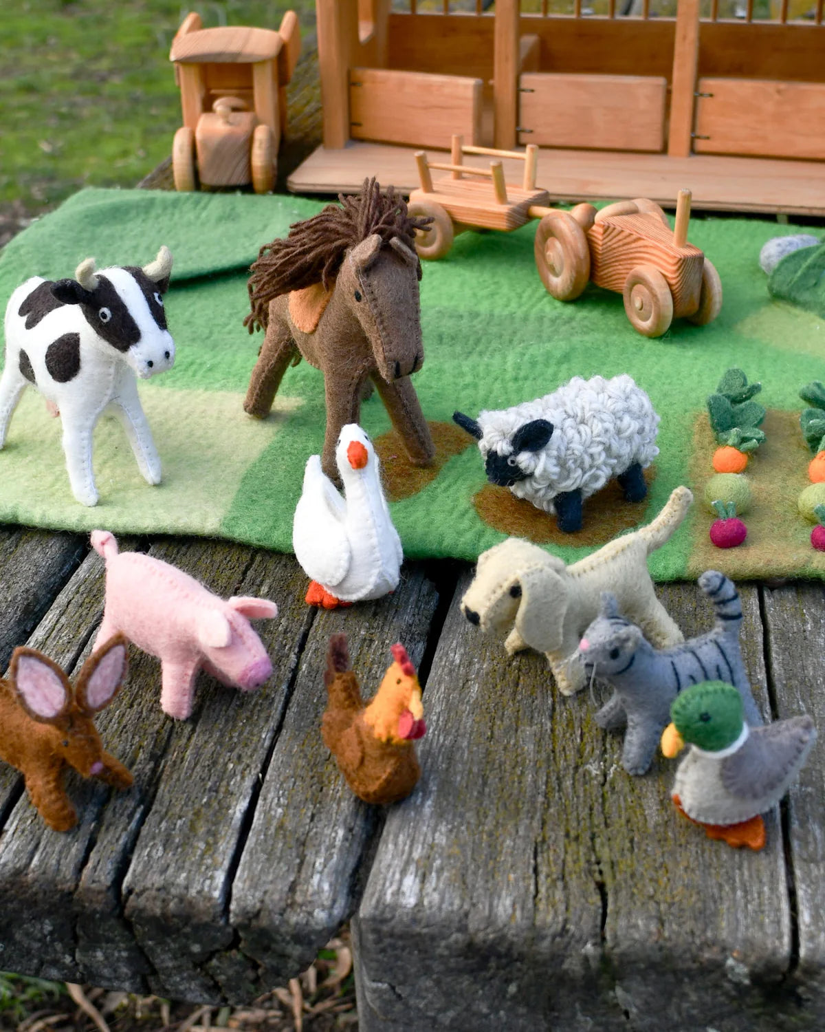 Toy farm animals on a wooden surface with a felt farm background