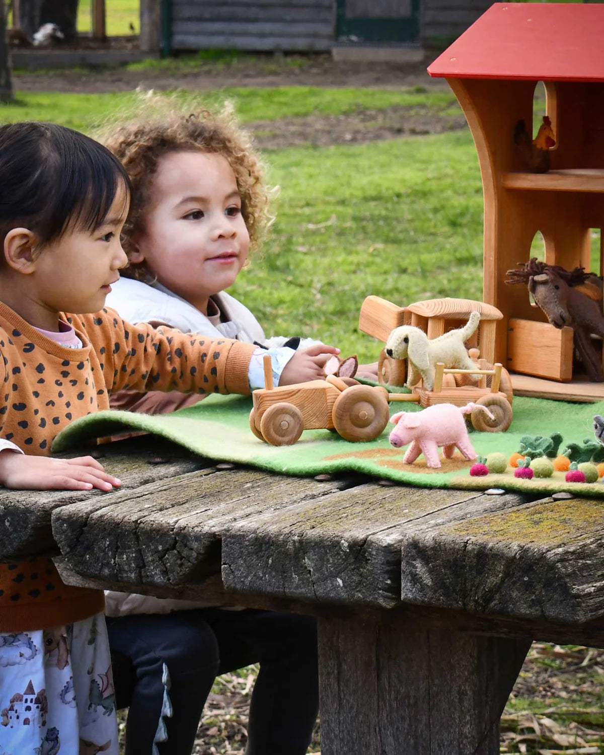 Two children playing with wooden toys on a blanket outdoors.