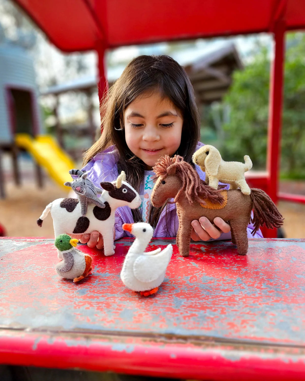 Child playing with toy animals on a red surface outdoors