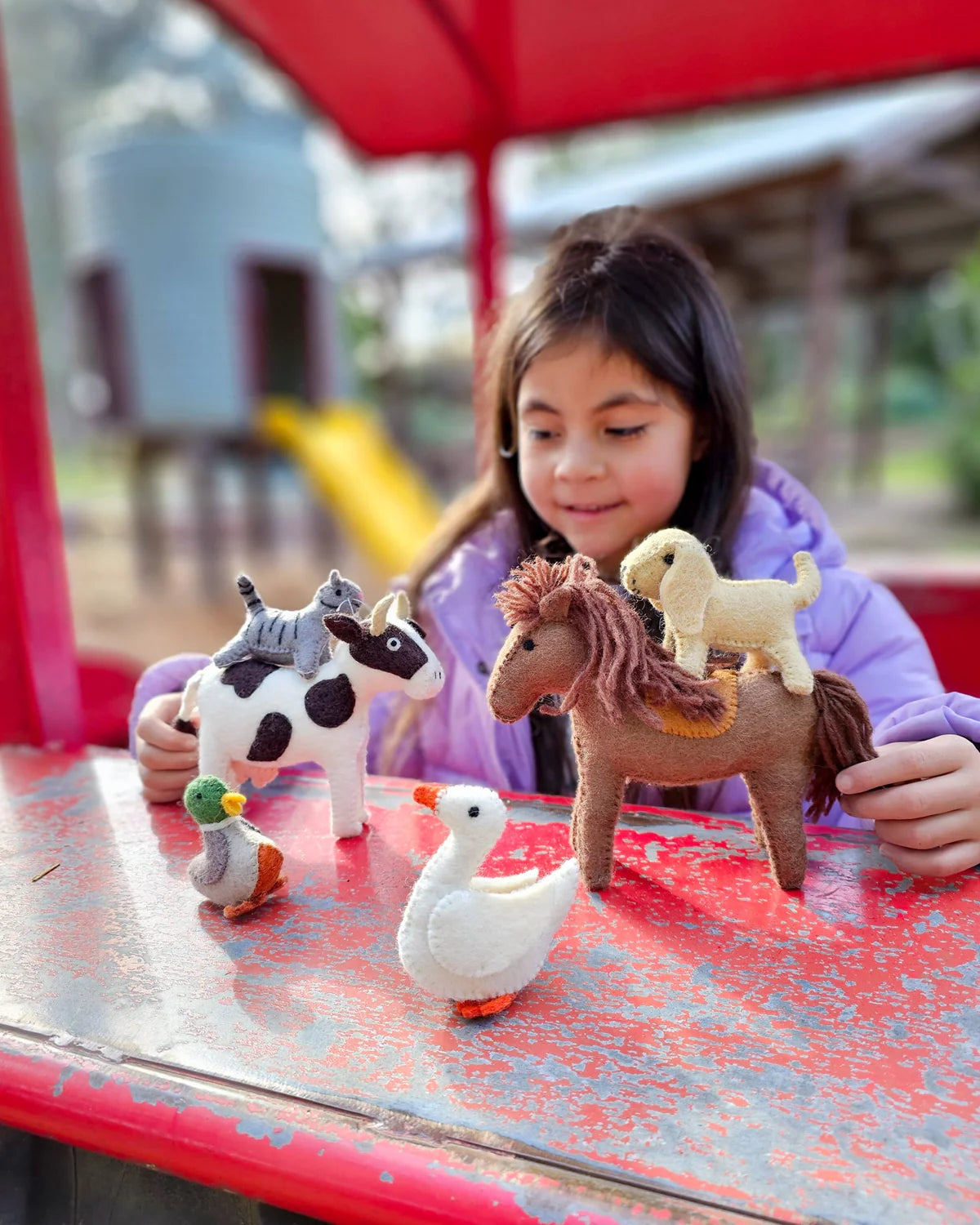 Child playing with toy animals on a red surface outdoors