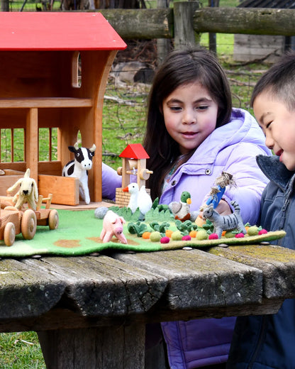 Two children playing with toy farm animals on a wooden table outdoors.