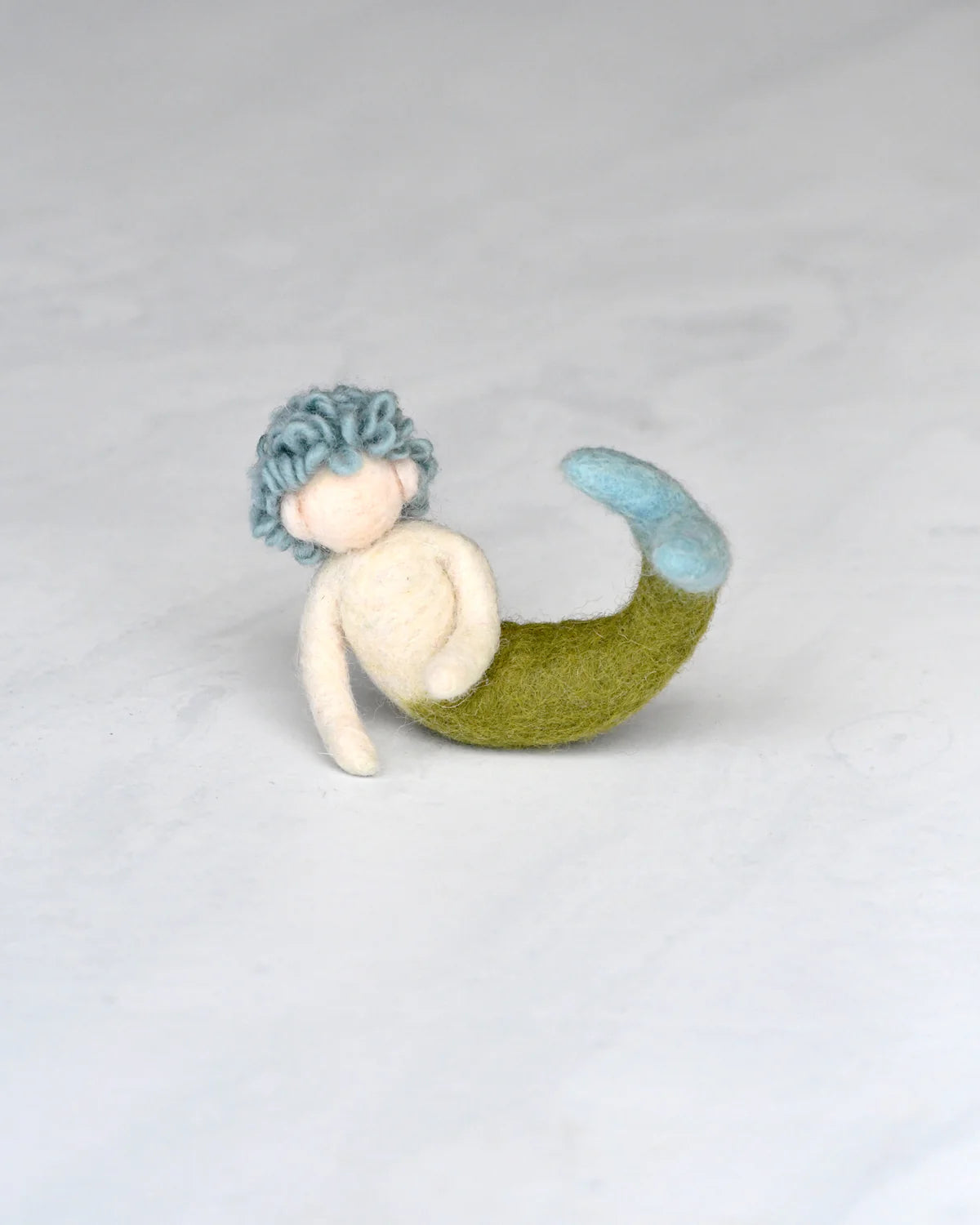 Mermaid toy with blue hair and green tail on a light gray background