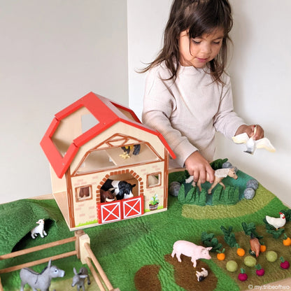 Child playing with a toy barn and farm animals on a green play mat.
