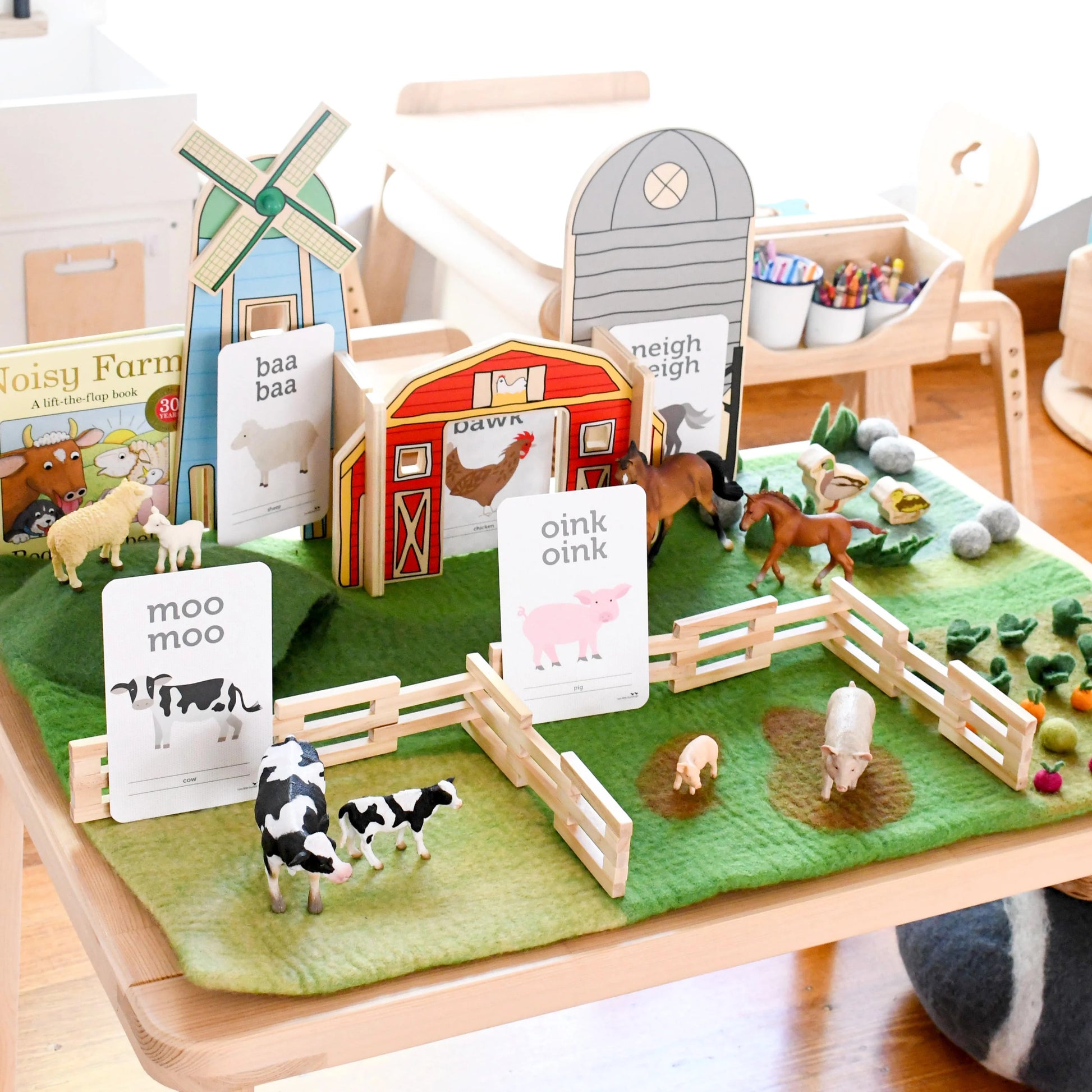 Toy farm set with animals, barn, and windmill on a green felt surface.