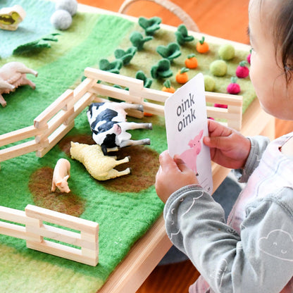 Child playing with a farm-themed toy set on a felt play mat