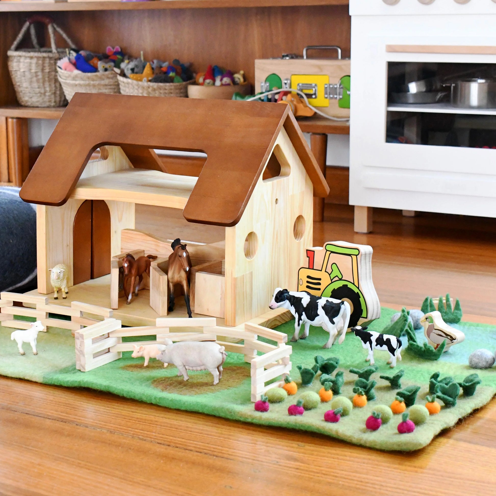 Wooden toy farm set with animals and a tractor on a green felt background.