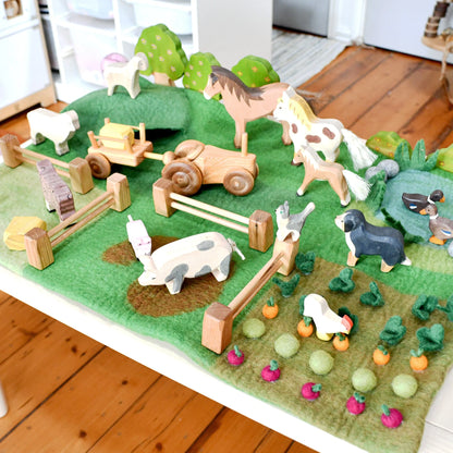 Wooden farm animals and structures on a green felt play mat.