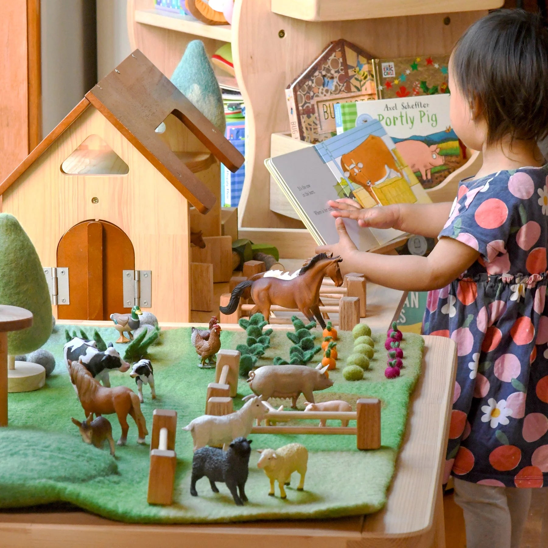 Child playing with a toy farm set and reading a book