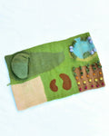 Felted landscape with green grass, brown path, and blue sky on a white background