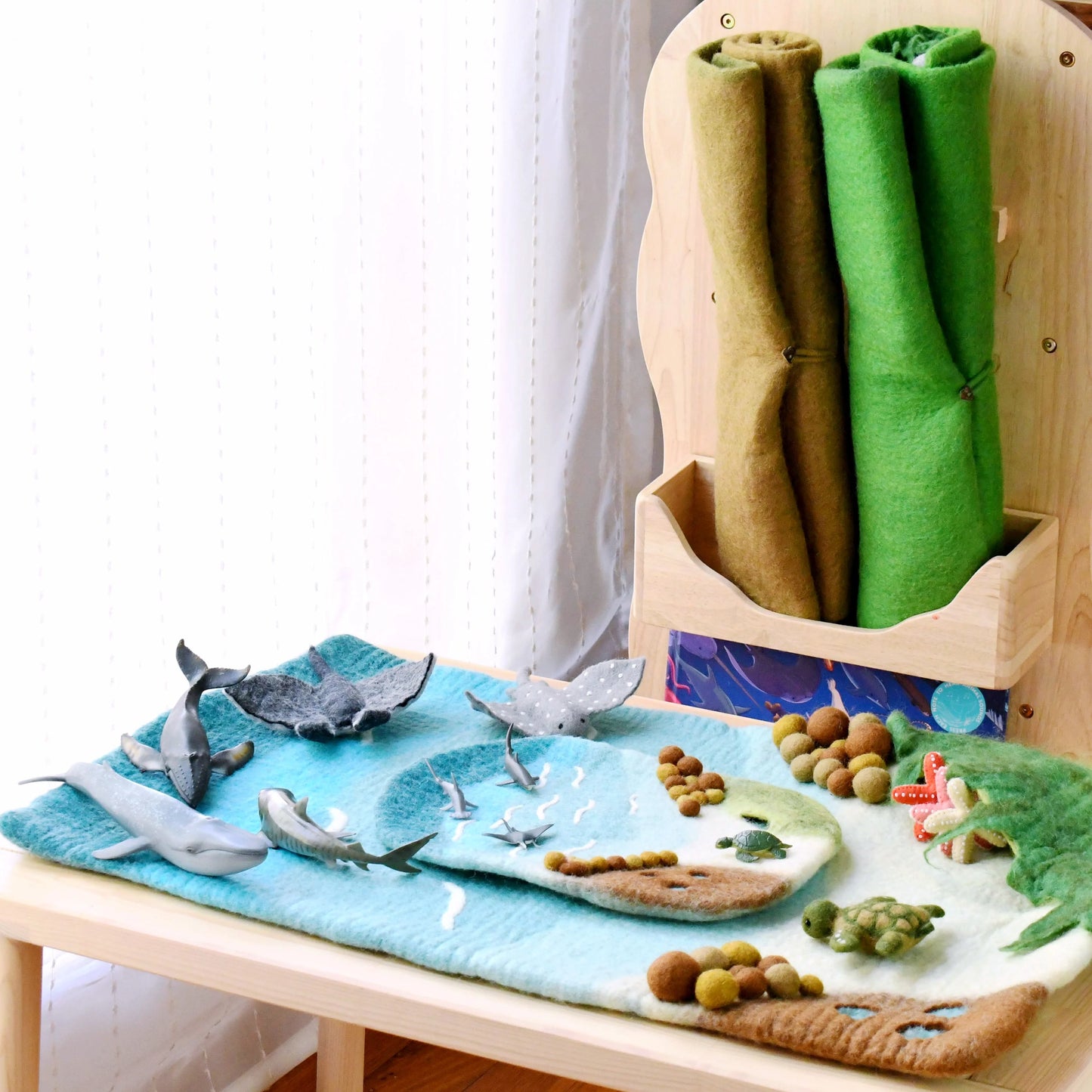 Children's play mat with toy sharks and sea creatures, accompanied by rolled-up fabric in a wooden holder.