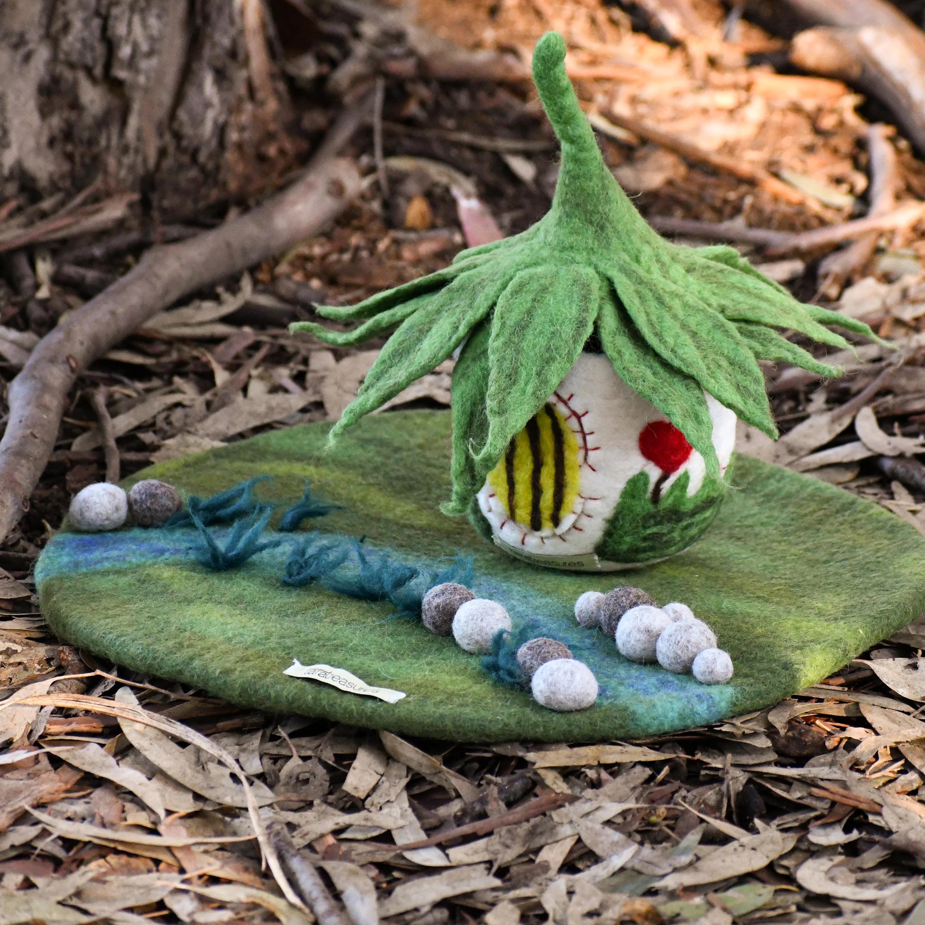 Felted garden scene with a small house on a leaf, surrounded by natural elements.