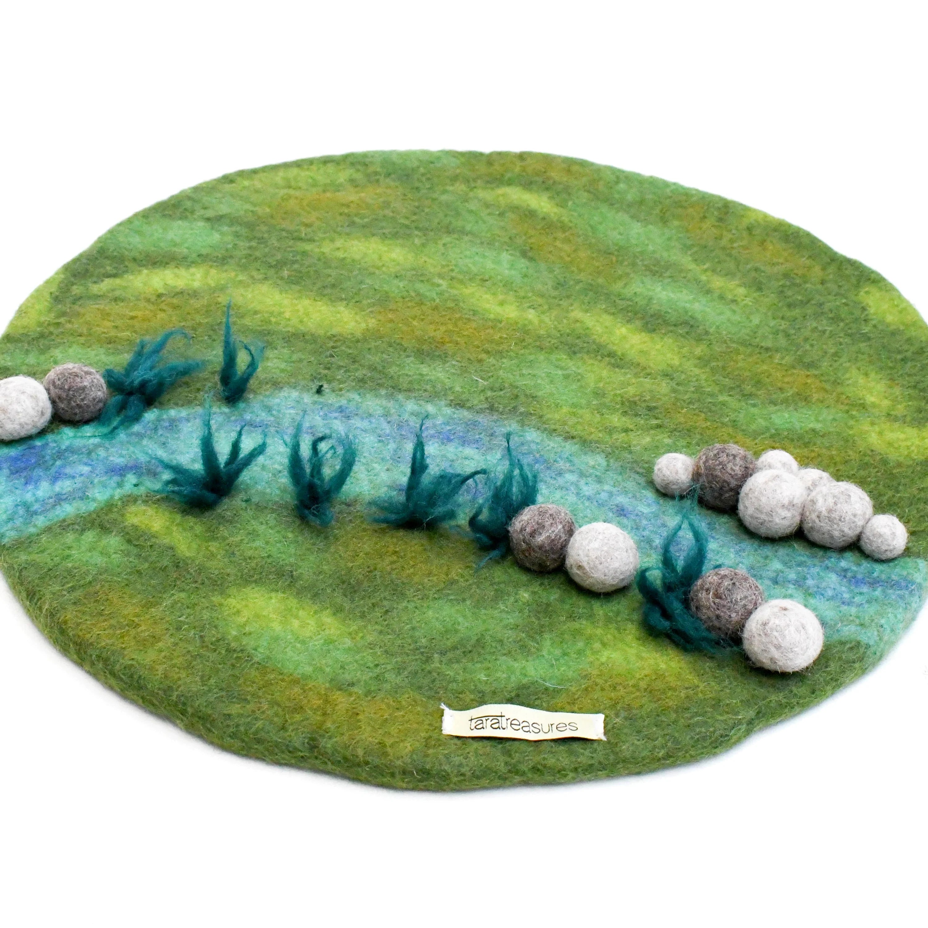 Felted landscape with grass, water, and rocks on a white background