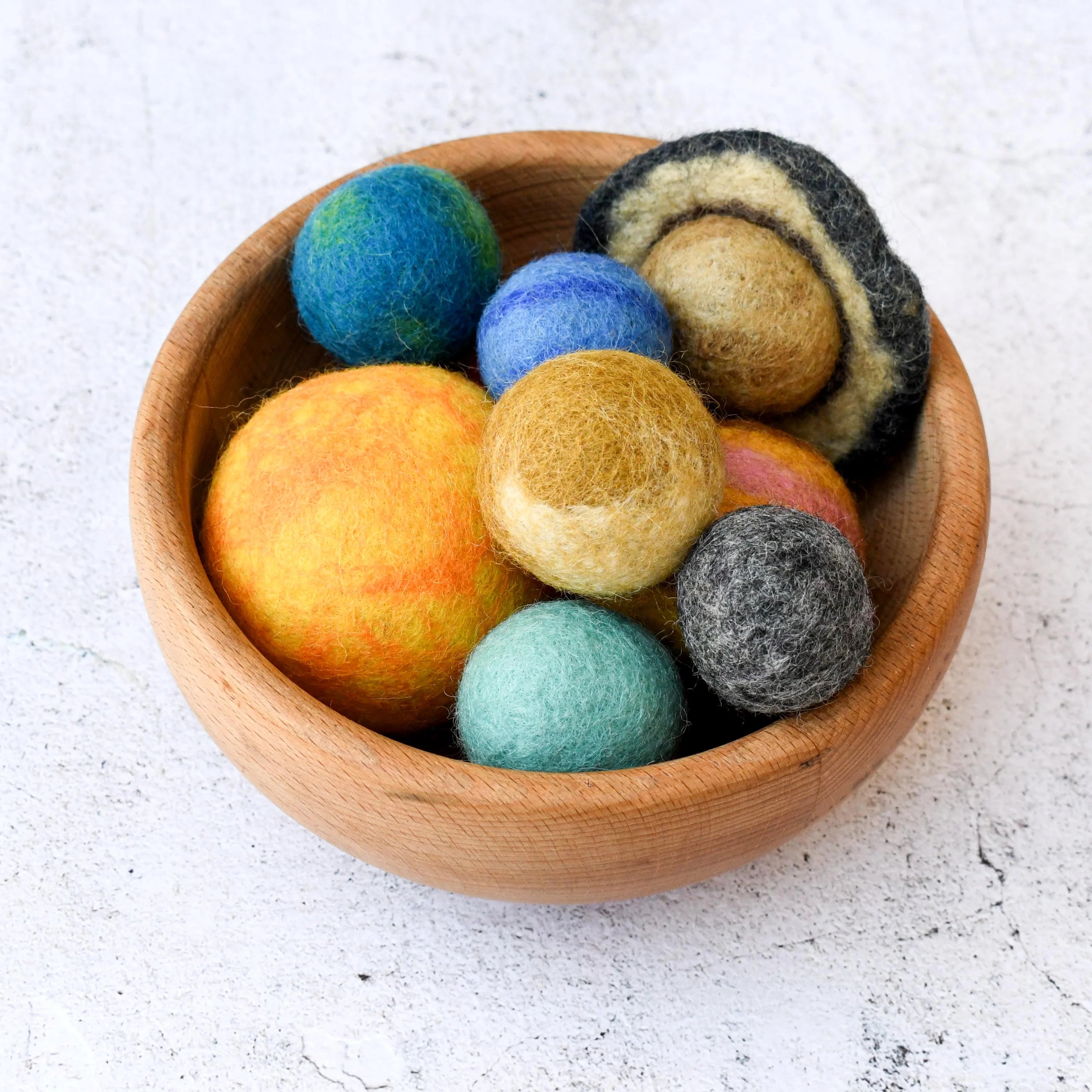Wooden bowl filled with colorful felt balls on a light background