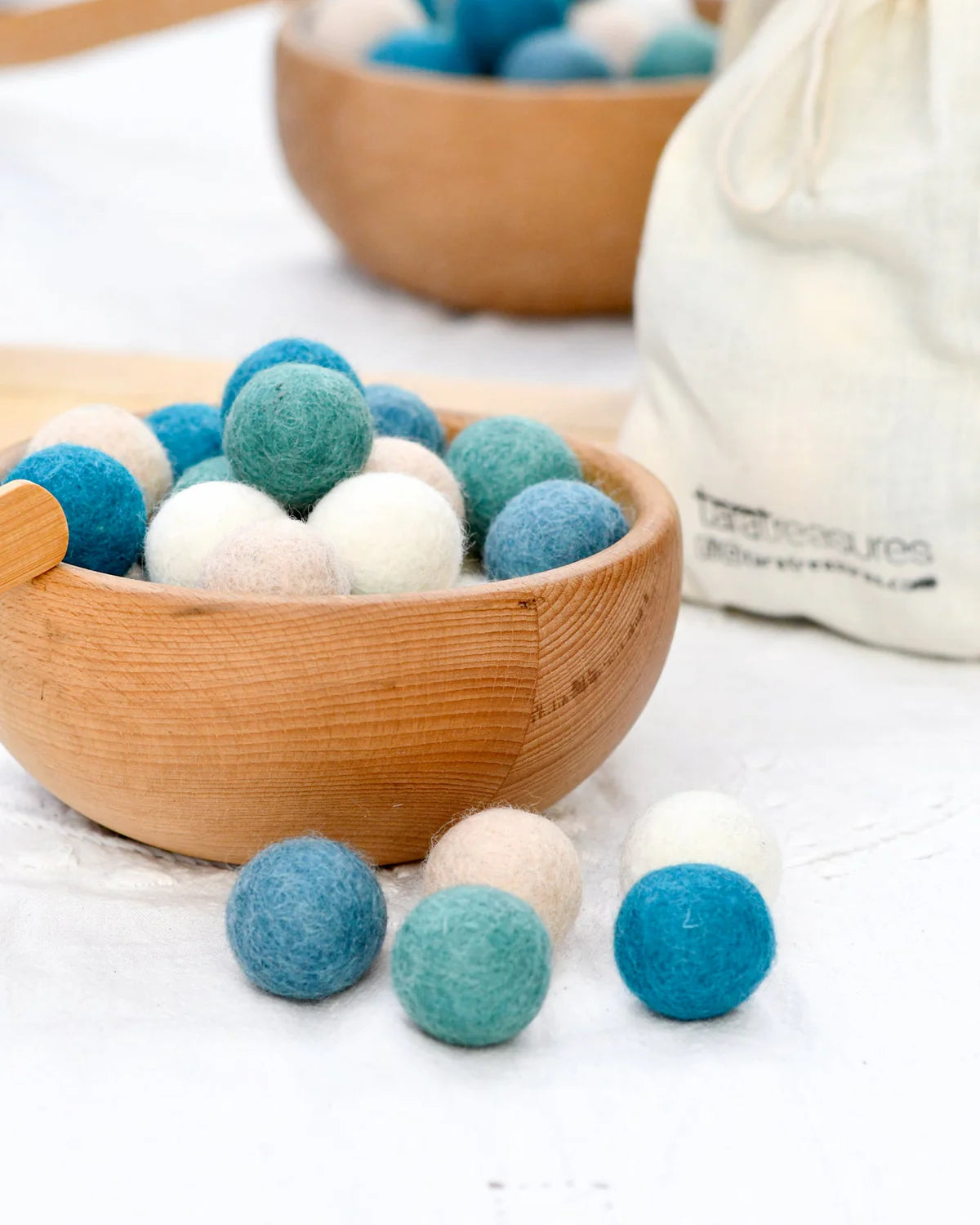 Wooden bowl filled with blue and white felt balls on a light surface.