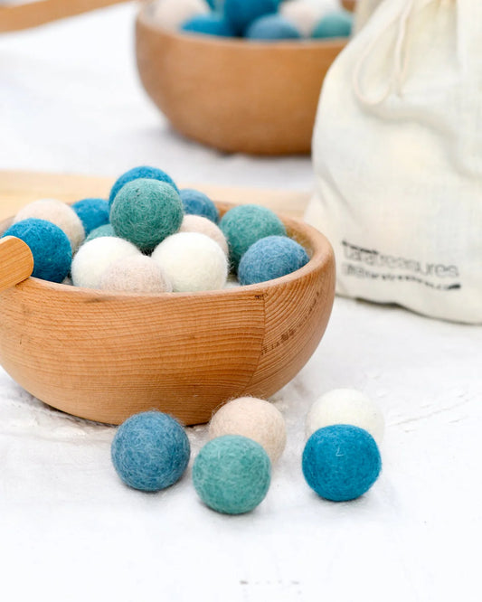 Wooden bowl filled with blue and white felt balls on a light surface.
