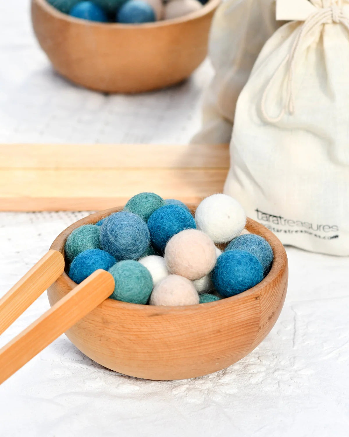 Wooden bowl with blue, green, and white felt balls on a light surface.