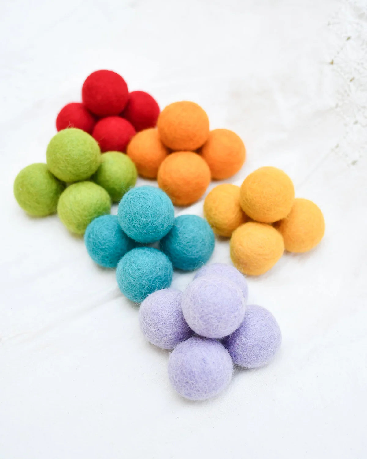 Colorful felt balls arranged in a rainbow pattern on a white background