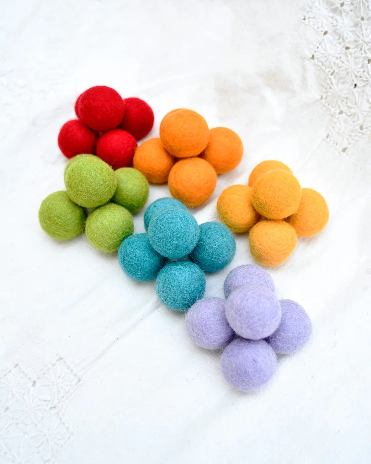 Colorful felt balls arranged in a rainbow pattern on a textured white surface.