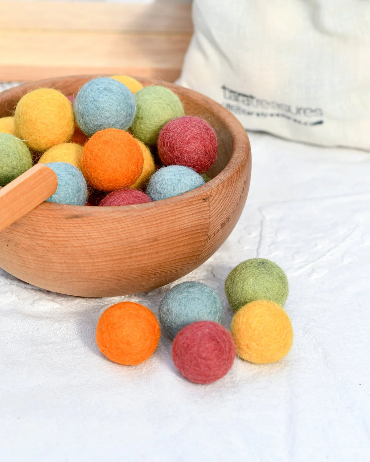 Colorful felt balls in a wooden bowl on a white surface