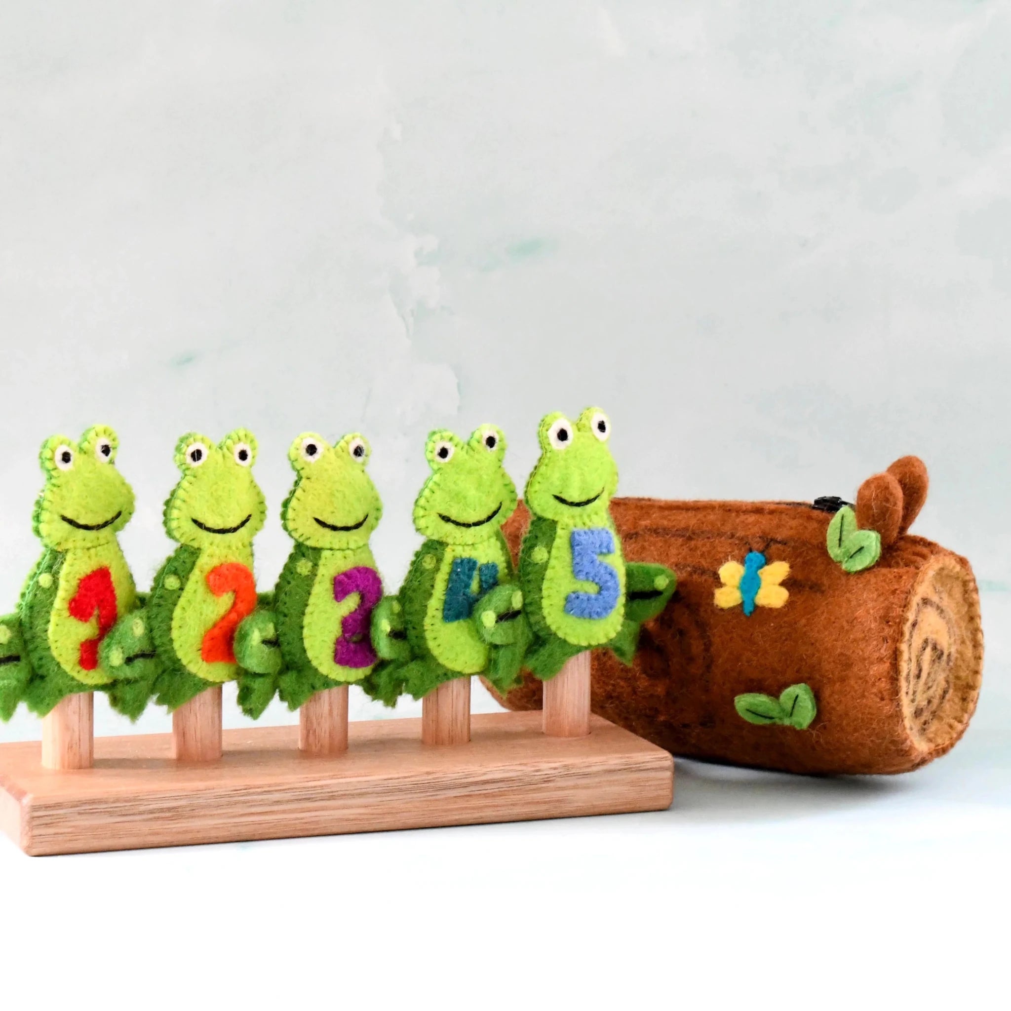 Set of green caterpillar-shaped numbers on a wooden stand with a brown log and butterfly decoration in the background.