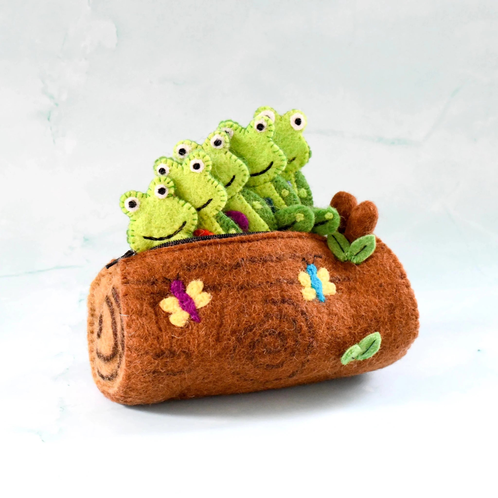Plush toy with green frogs on a brown log against a light background