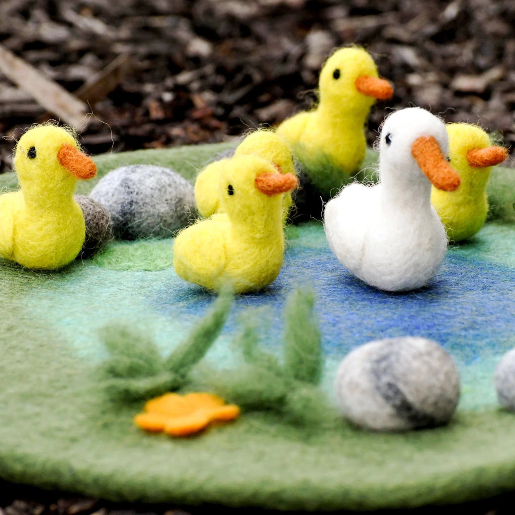 Felted toy ducks and goose on a felt pond with rocks and plants.