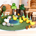 Felt playset with ducks, trees, and a pond on a green felt surface.