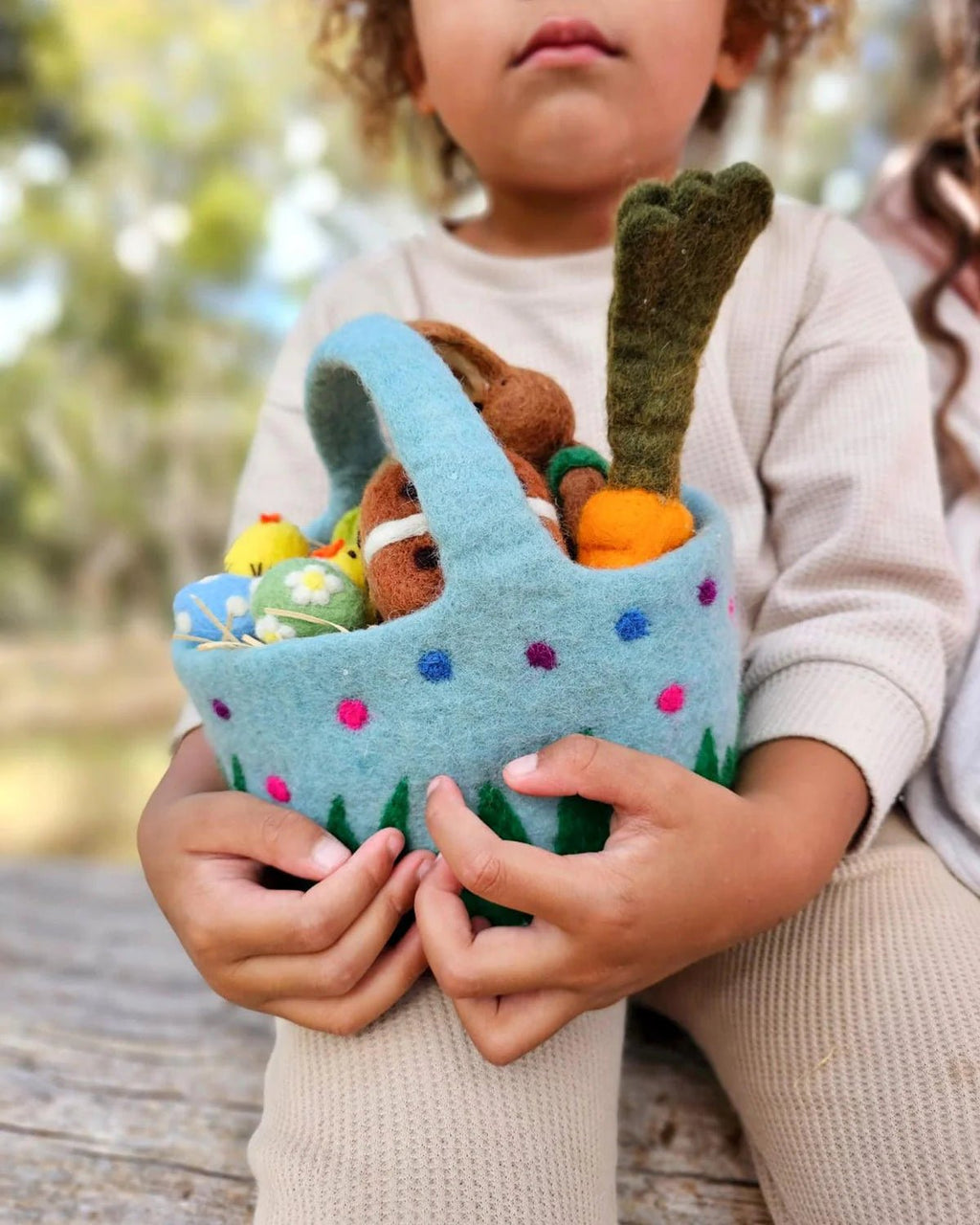 Child holding a felt Easter basket with toys outdoors
