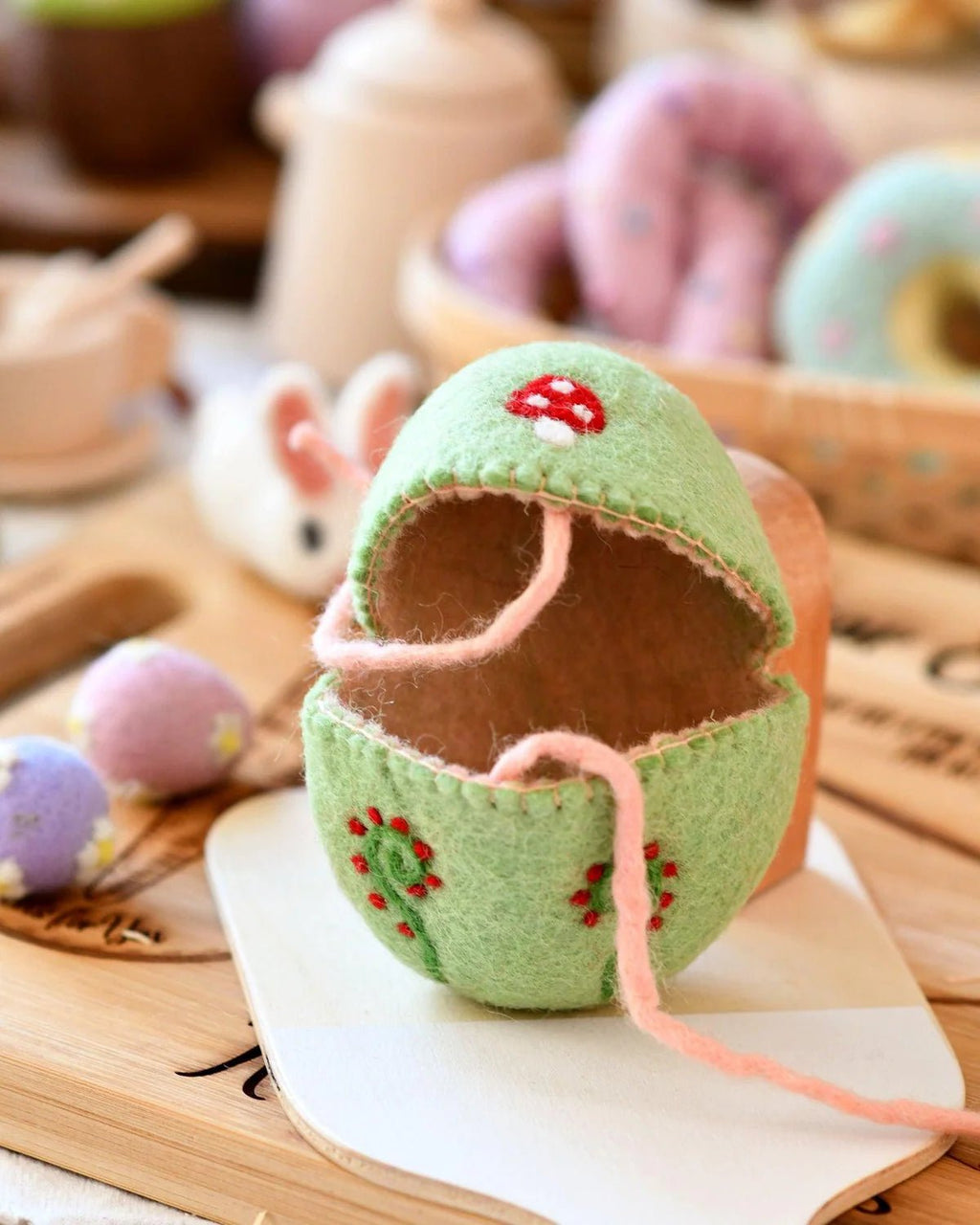 Green knitted egg-shaped toy with pink string on a wooden surface