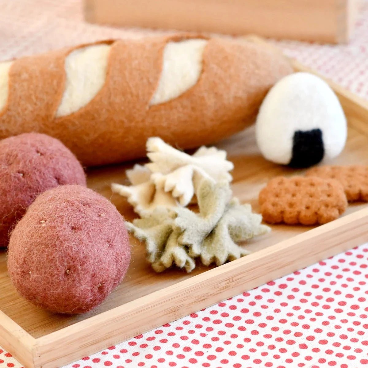 Wooden tray with sea-themed items including a shell, red and pink spherical objects, and a black and white cylindrical object on a polka dot fabric background.