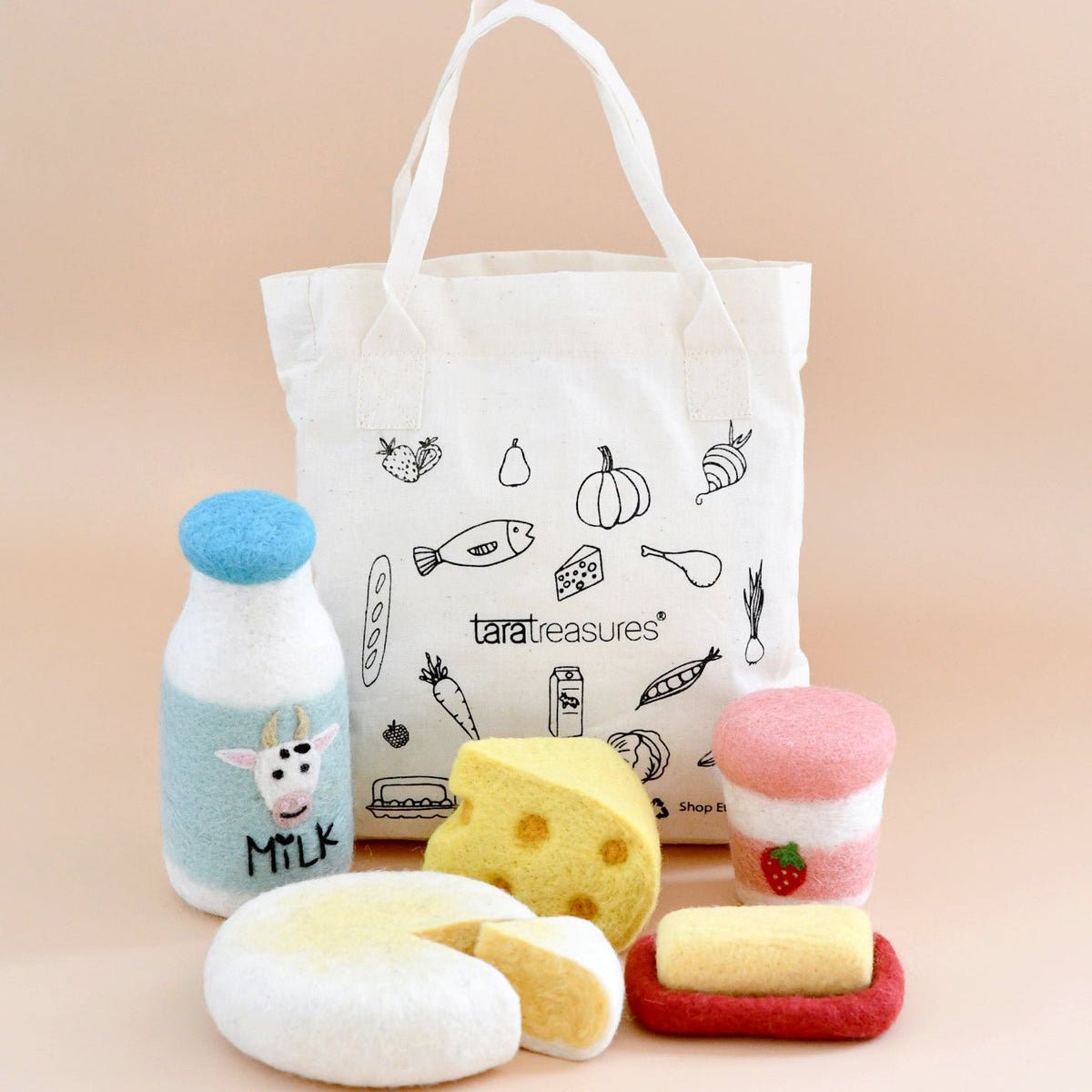 Toy food items including a bottle, cheese, and bread on a beige background with a tote bag featuring illustrations and text.