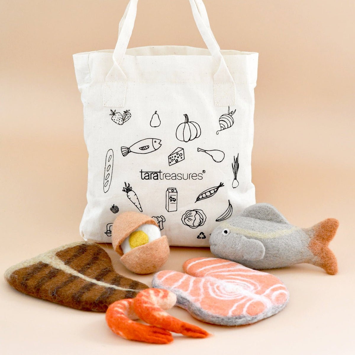White tote bag with black illustrations and text, accompanied by toy food items on a beige background