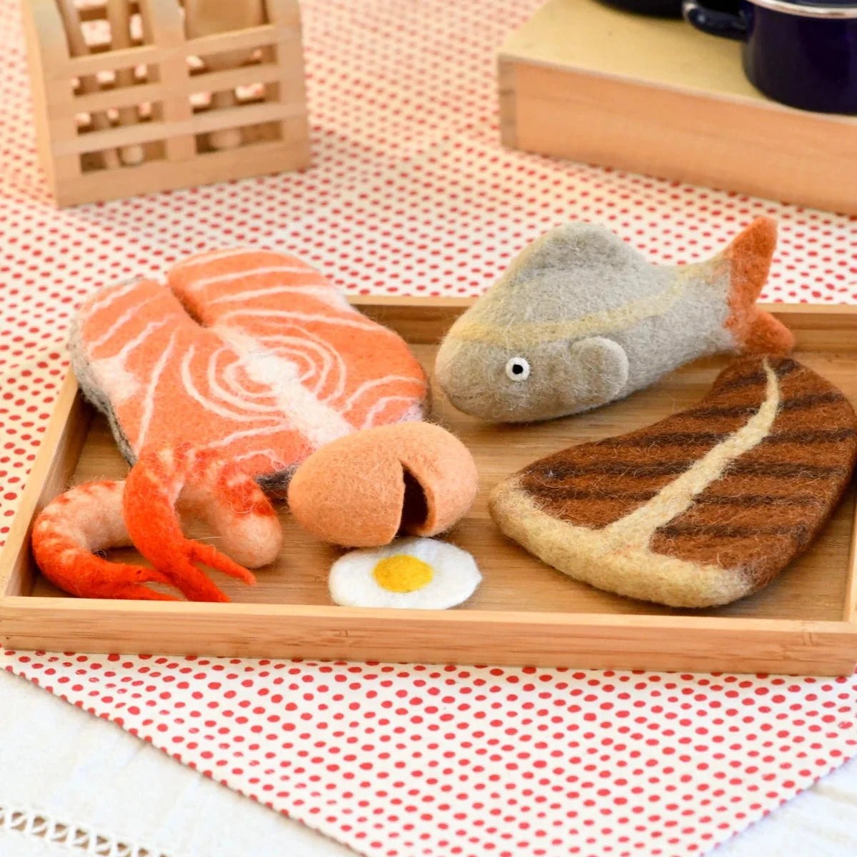 Toy food items including fish, salmon, and bread on a wooden tray with a red and white checkered tablecloth.