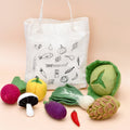 Tote bag with vegetable illustrations and felt vegetable toys on a beige background
