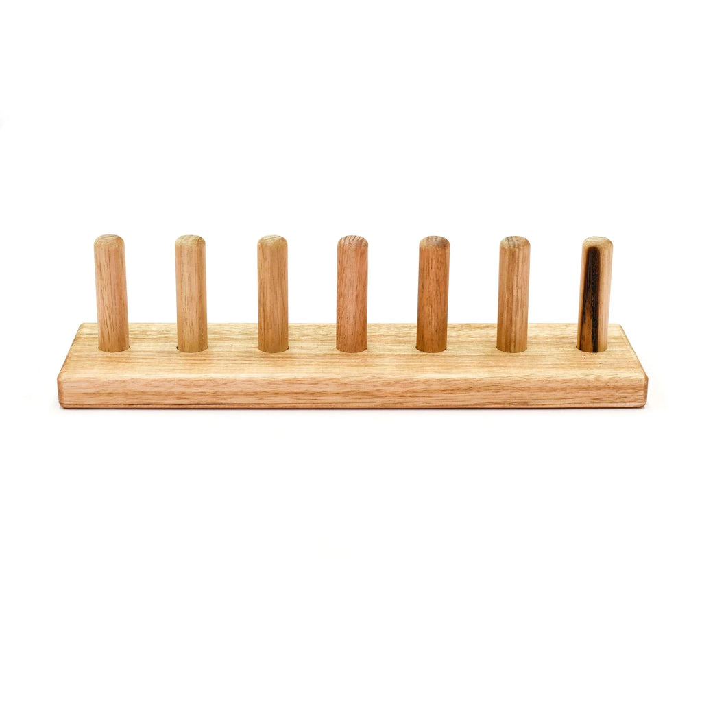 A natural wood menorah with seven upright pegs on a rectangular base, shown against a plain white background.