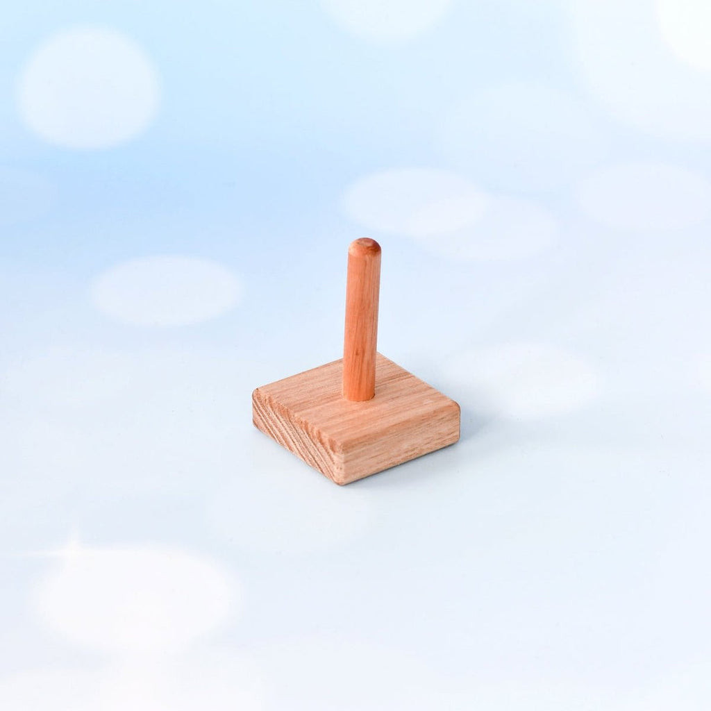 A small wooden toy or stand with a square base and a single upright post, photographed against a soft light blue and white bokeh background.