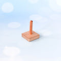 A small wooden toy or stand with a square base and a single upright post, photographed against a soft light blue and white bokeh background.