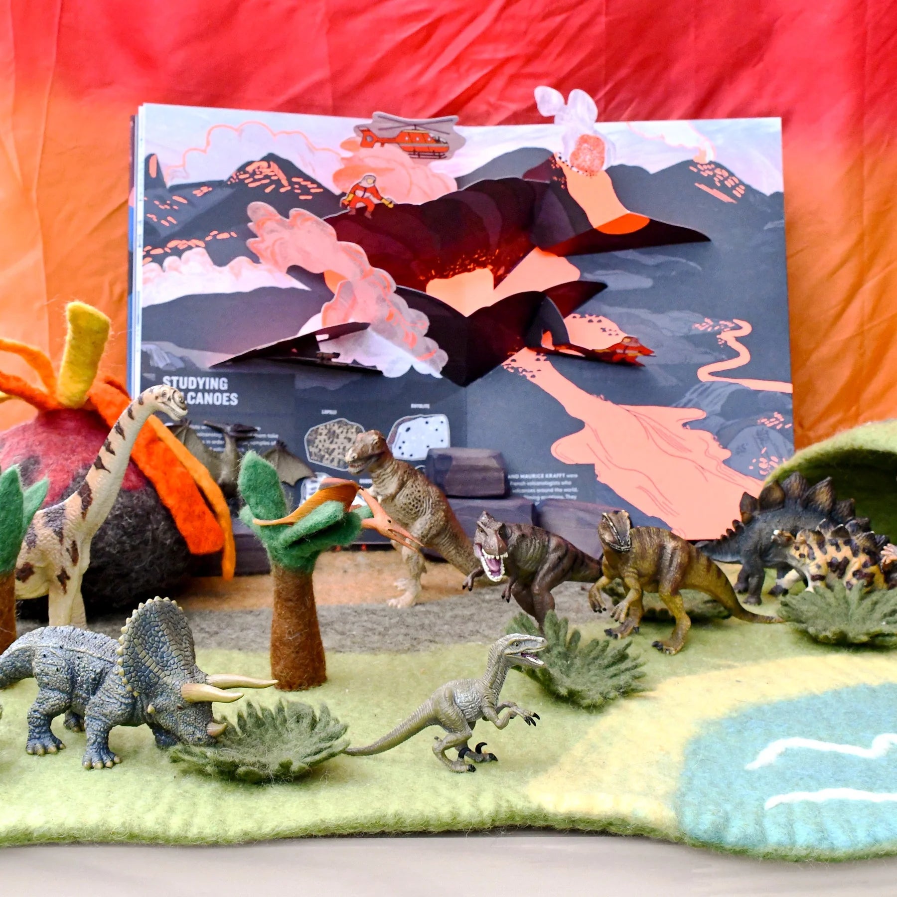 Dinosaur toys on a colorful felt play mat with a pop-up book in the background