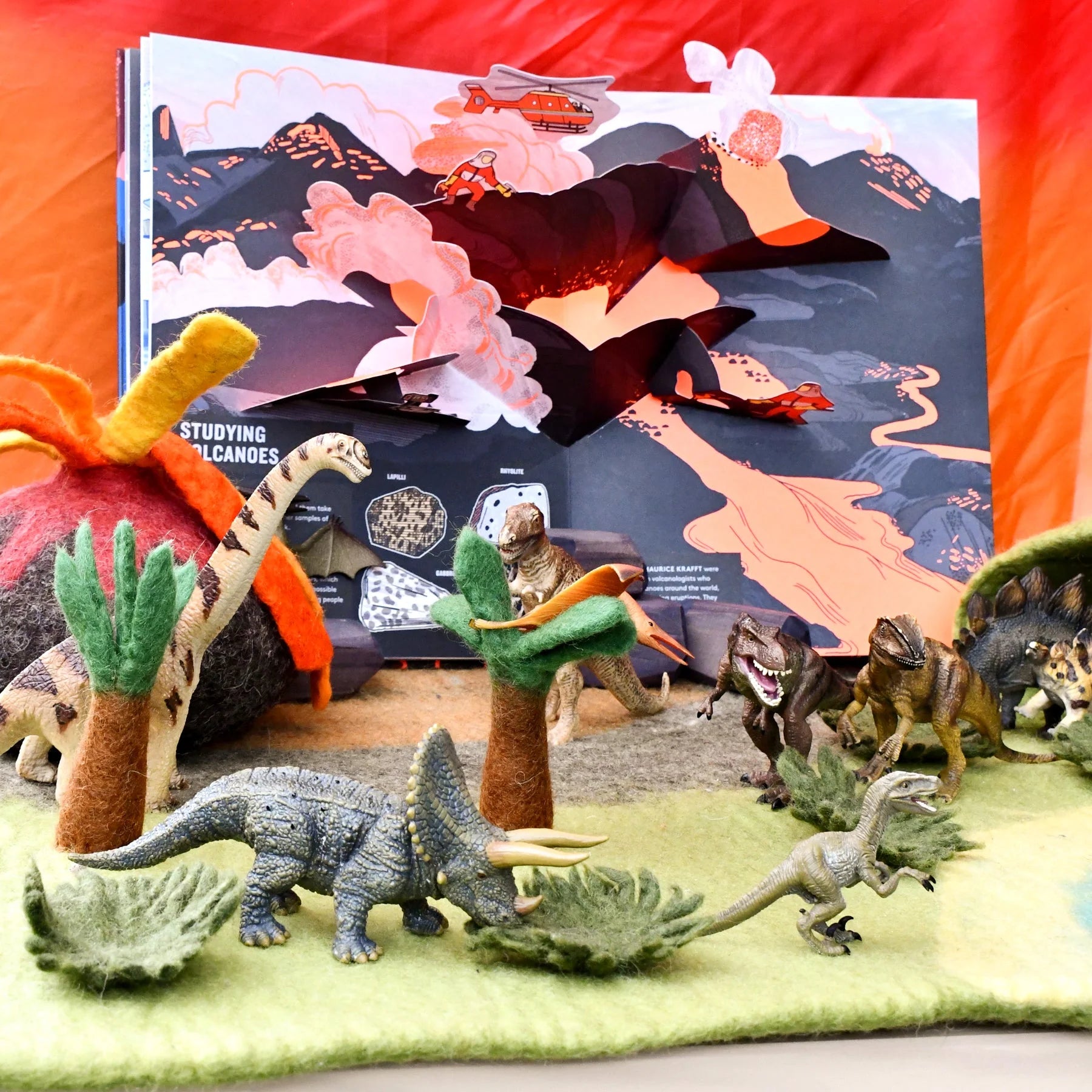 Dinosaur toys and a pop-up book set against a red background