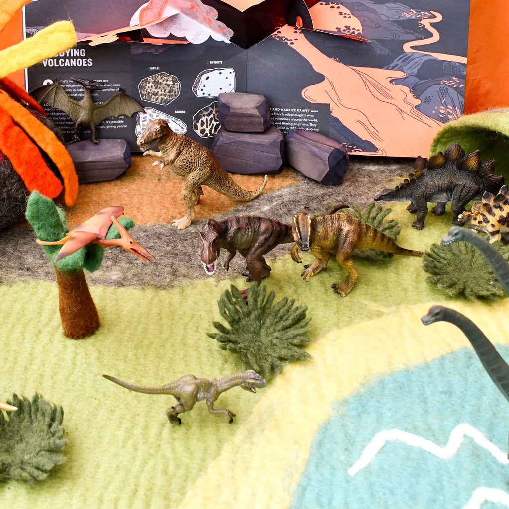 Toy dinosaurs and landscape setup with educational book in the background