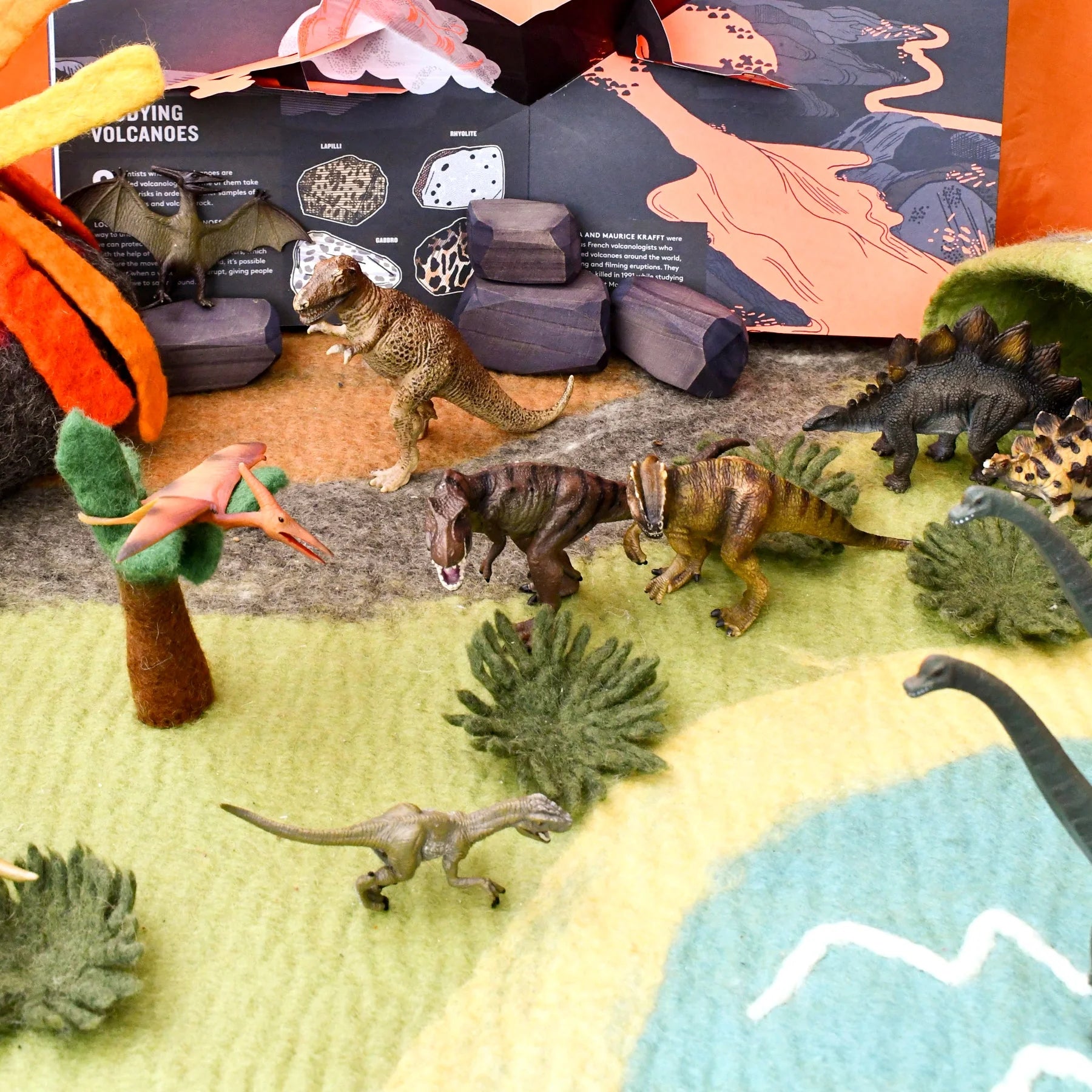 Toy dinosaurs and landscape setup with educational book in the background