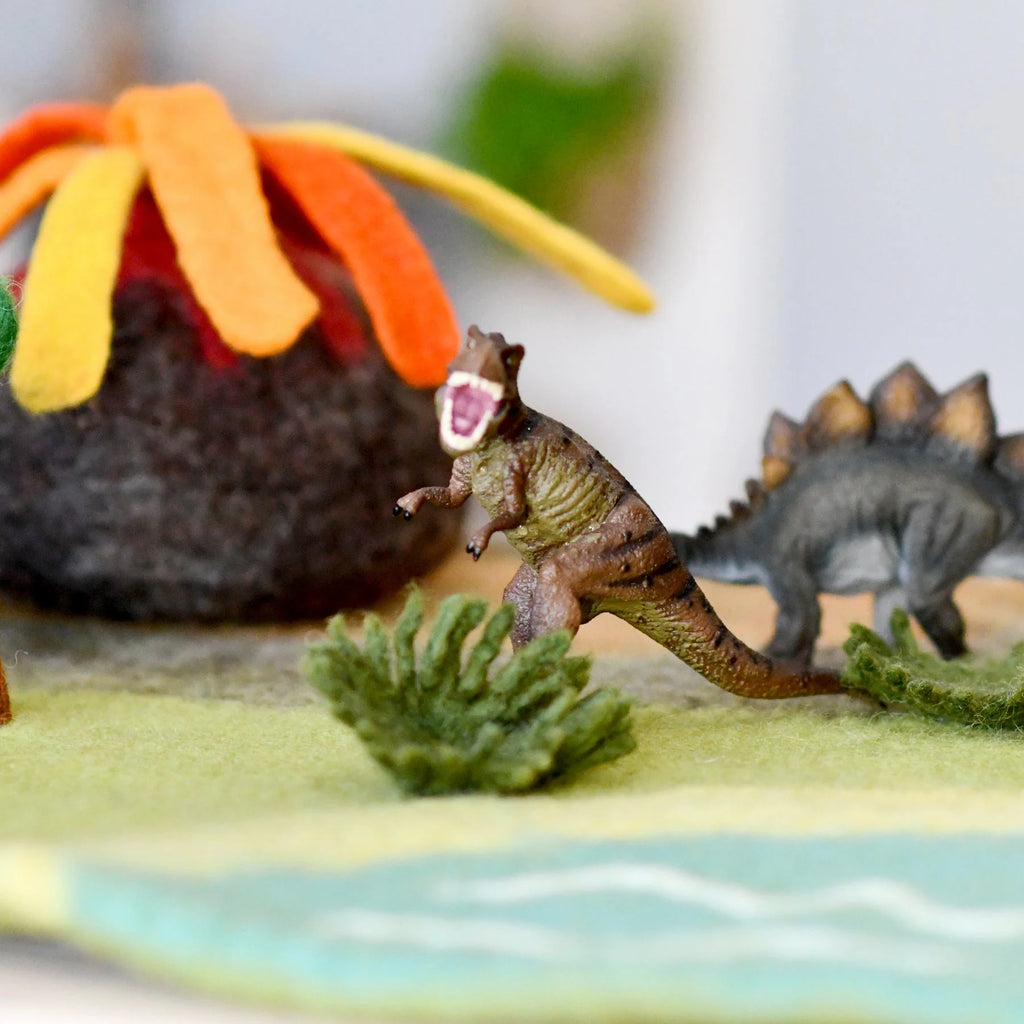 Toy dinosaurs on a felt landscape with a volcano and water body.