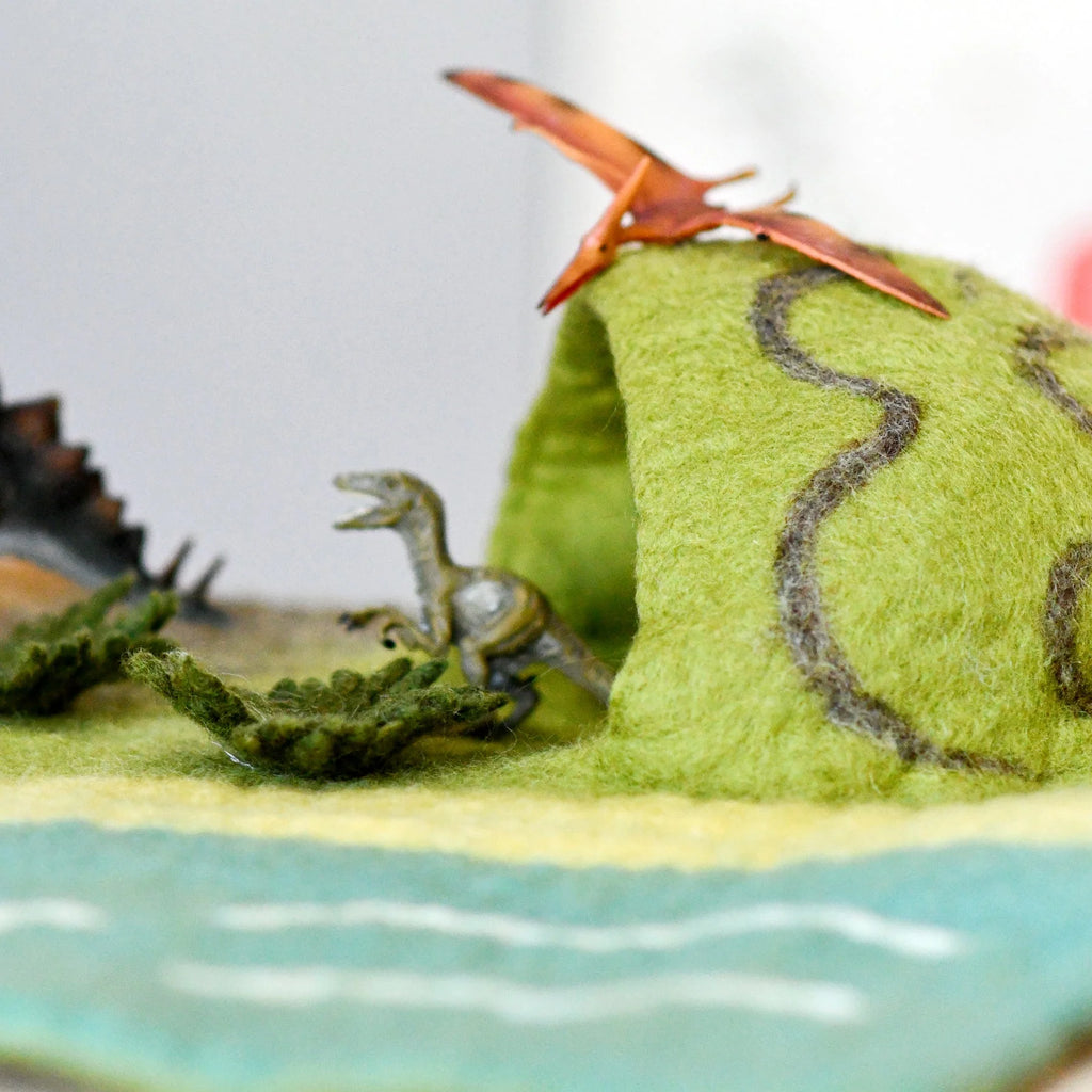 Model of a dinosaur and a pterodactyl on a green landscape with water.