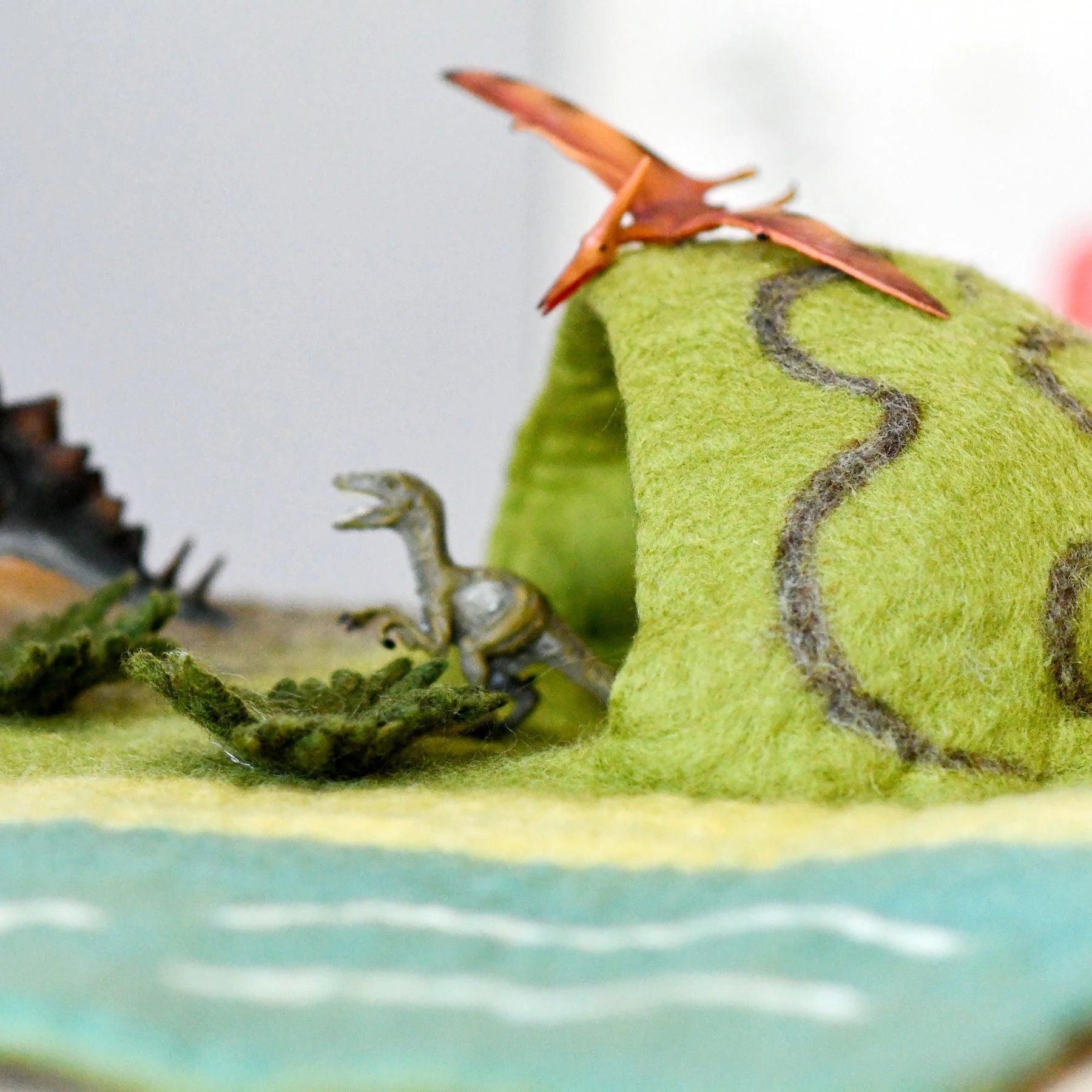 Model of a dinosaur and a pterodactyl on a green landscape with water.