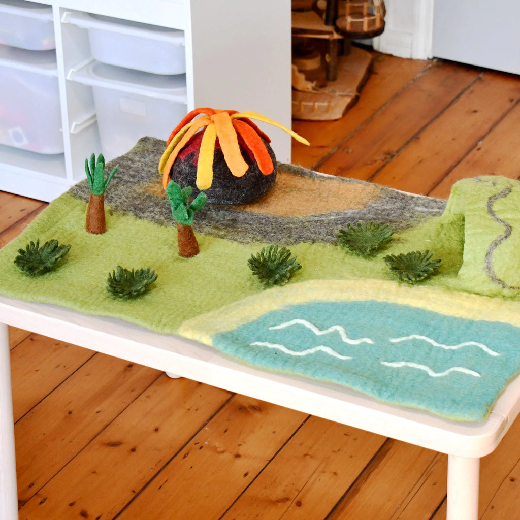 Felted landscape with trees and a mountain on a white surface.