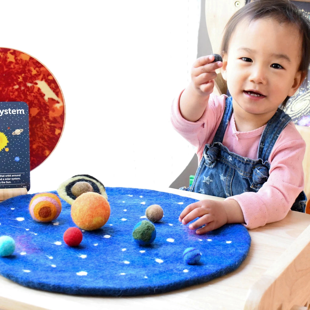 Child playing with a solar system model on a blue felt surface
