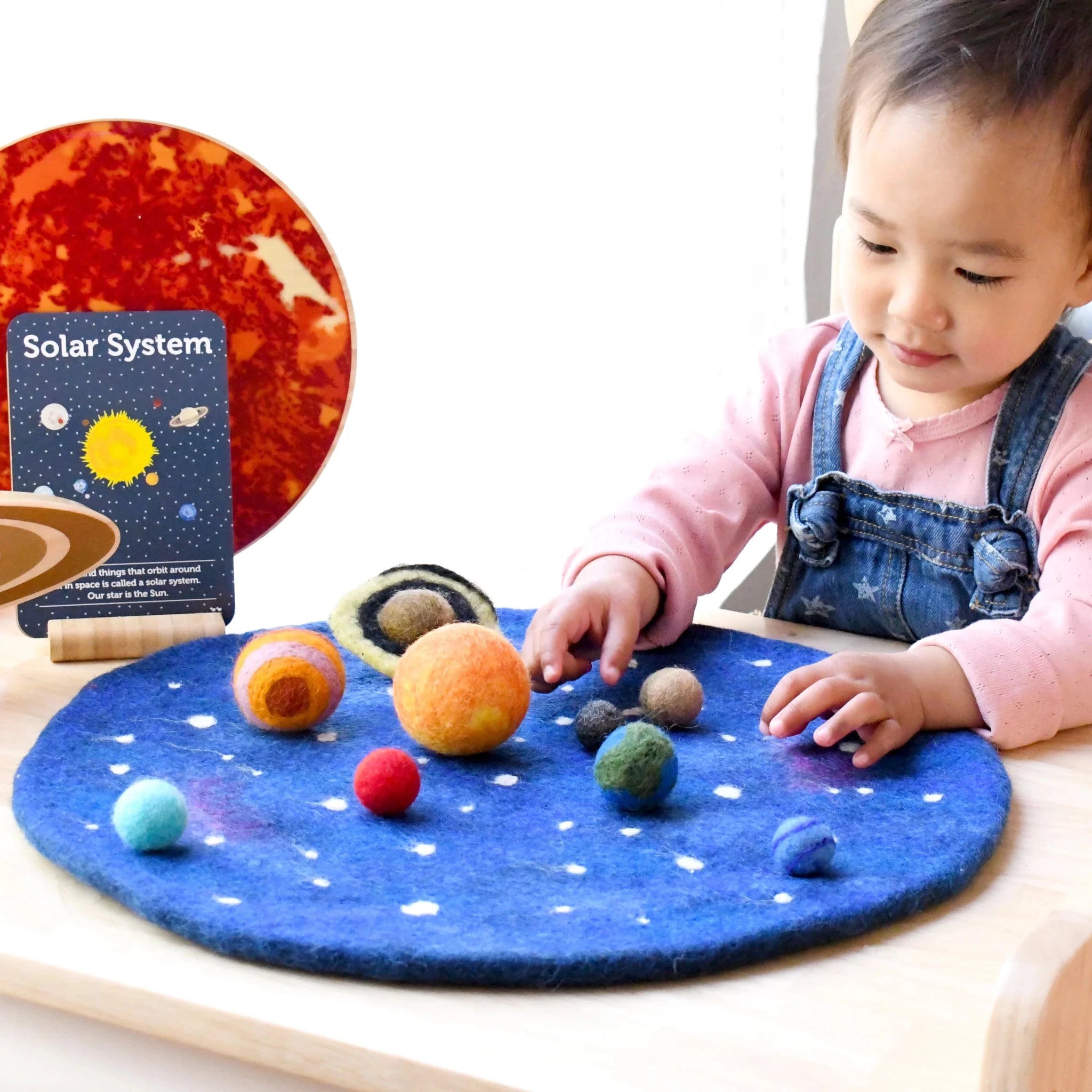 Child playing with a solar system toy set on a felt surface