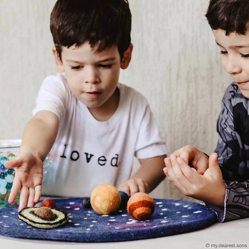 Two children playing with toy planets on a starry surface.