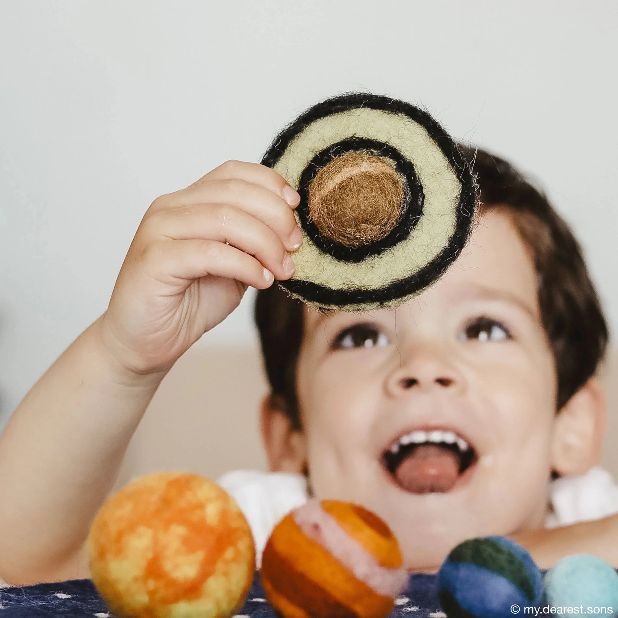 Child holding a felt planet model with a plain background
