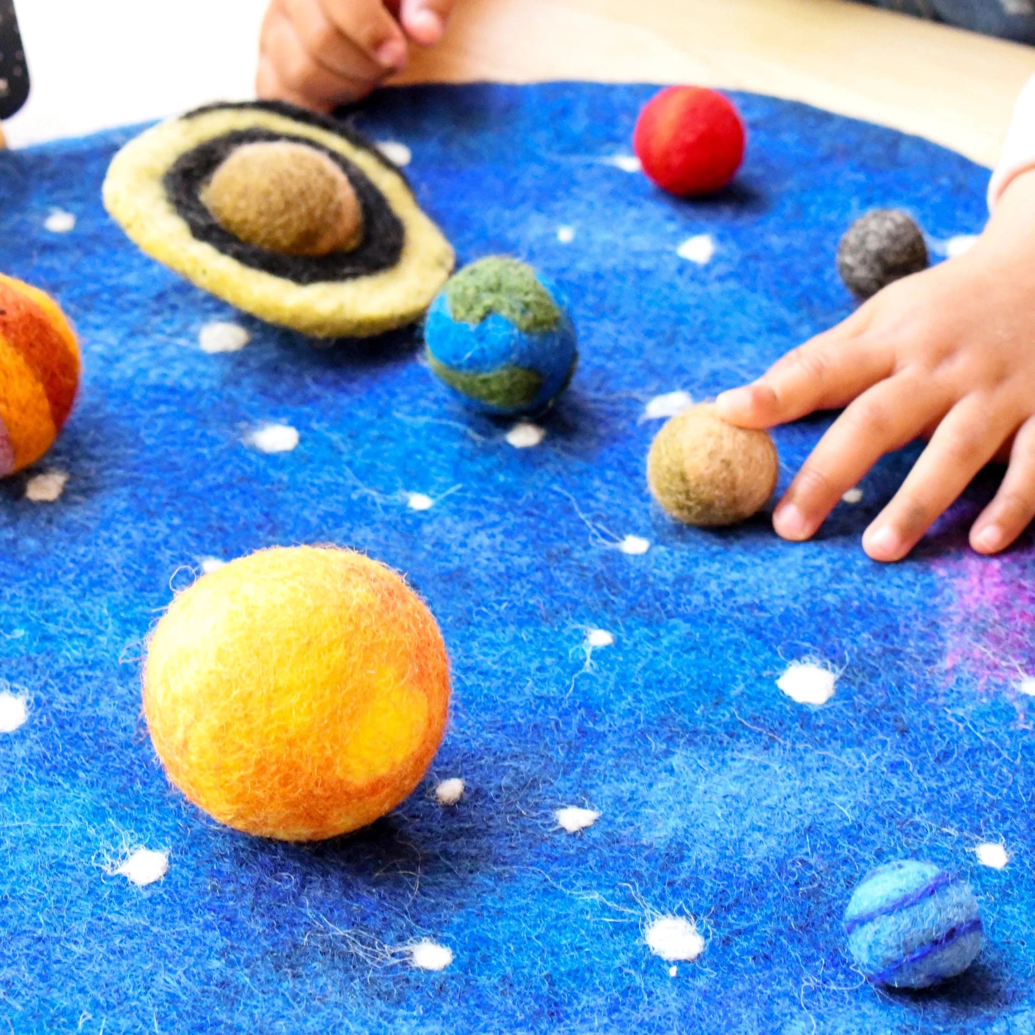Children's hands interacting with felt solar system model on a blue surface